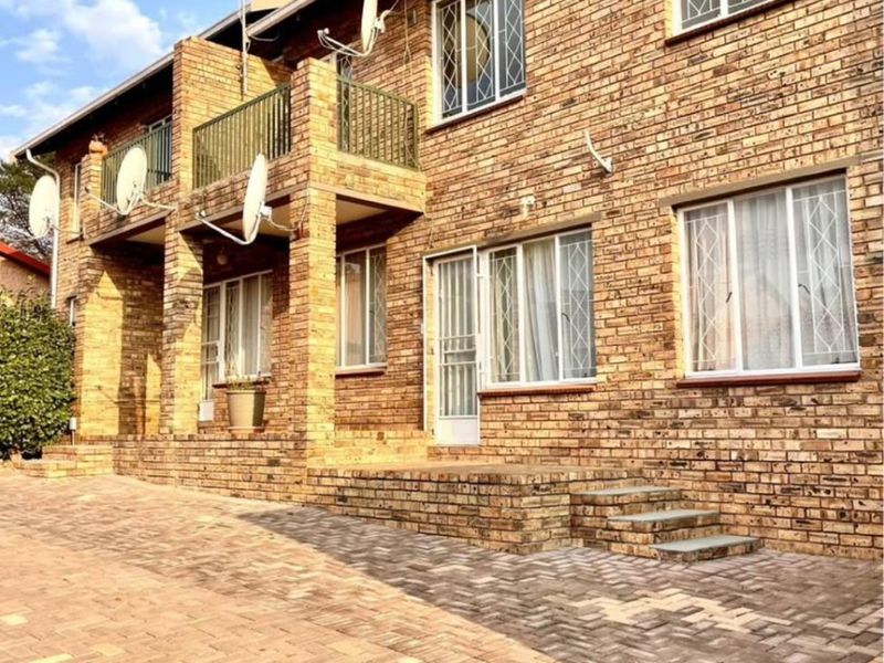 A well-maintained face brick townhouse exterior featuring a paved driveway, balcony, and secure window and door fittings.