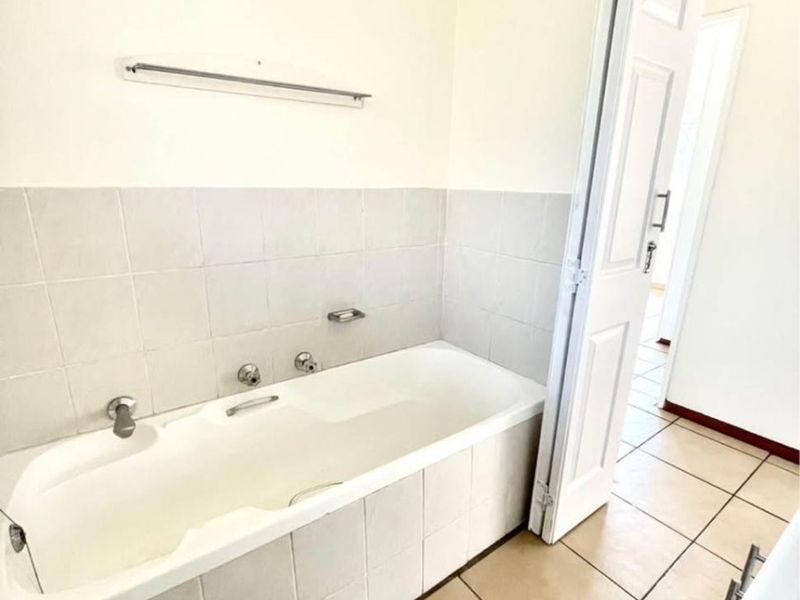 A functional bathroom featuring a built-in bathtub with tiled surround, ceramic floor tiles, and neutral wall finishes.