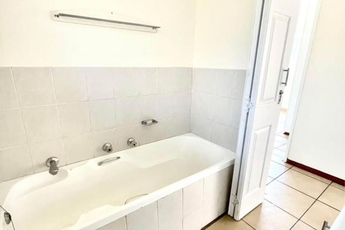 A functional bathroom featuring a built-in bathtub with tiled surround, ceramic floor tiles, and neutral wall finishes.