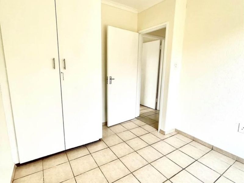 A clean, empty bedroom featuring neutral ceramic floor tiles, built-in wardrobe storage, and coved cornicing, offering a blank canvas for personalization.