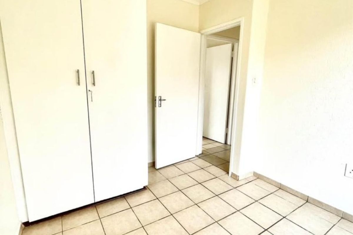 A clean, empty bedroom featuring neutral ceramic floor tiles, built-in wardrobe storage, and coved cornicing, offering a blank canvas for personalization.