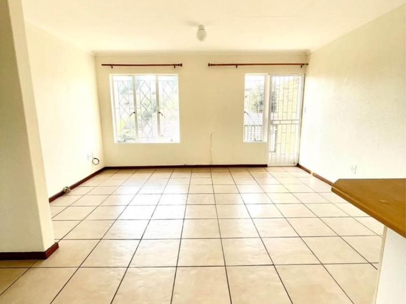 An empty, open-plan living area featuring neutral ceramic floor tiles, security bars on windows, and a breakfast counter, offering a blank canvas for interior design.