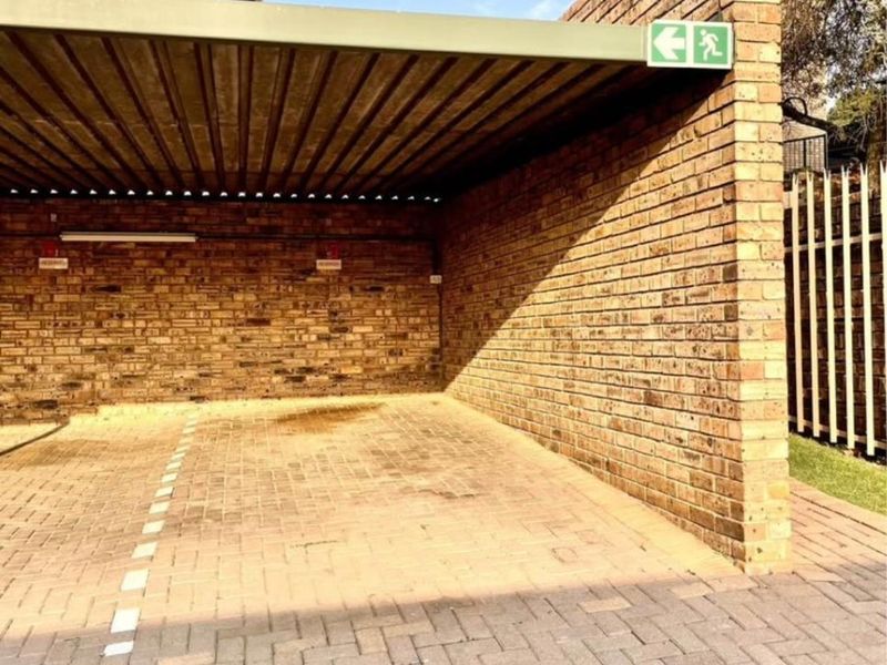 A covered carport area featuring brick walls and paved flooring, providing secure off-street parking for the townhouse.