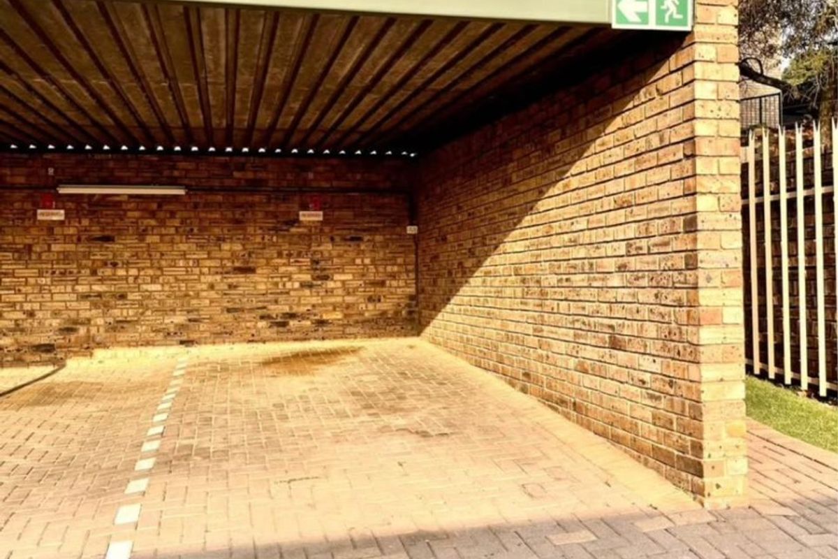 A covered carport area featuring brick walls and paved flooring, providing secure off-street parking for the townhouse.