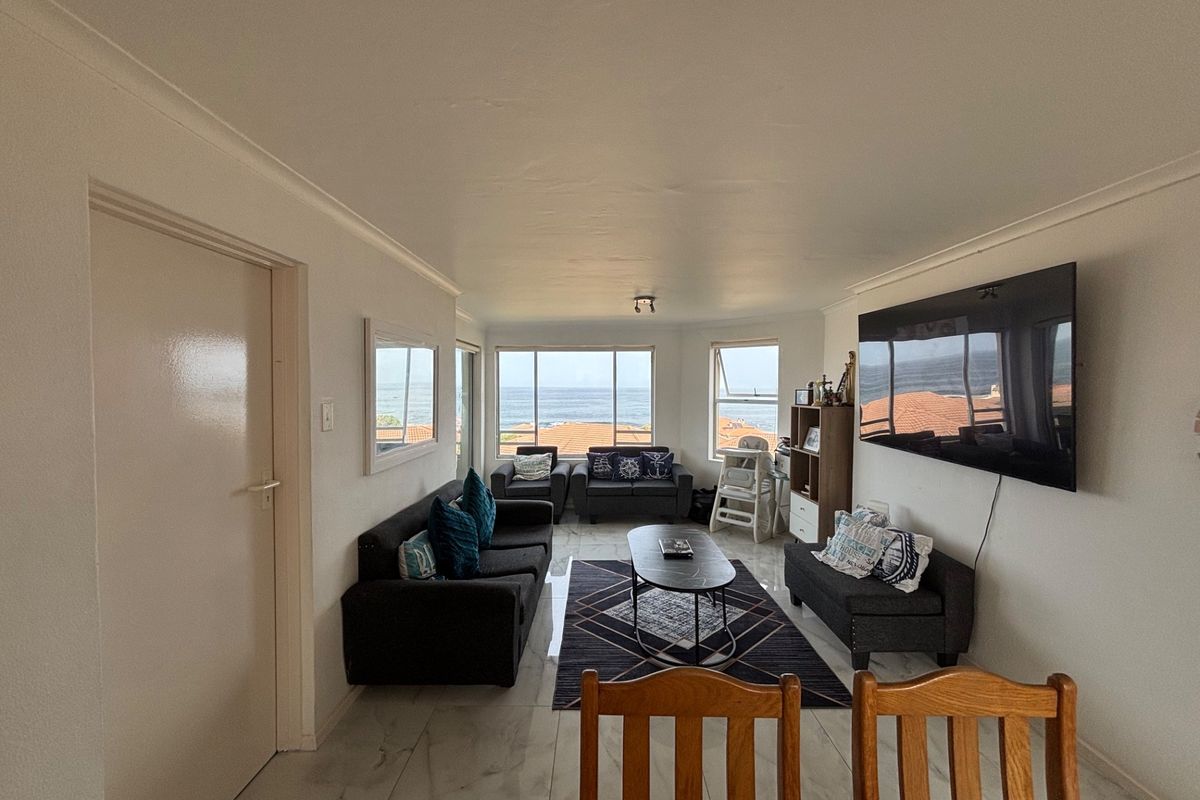 A bright living room featuring tiled flooring, coved ceilings, and large windows offering scenic ocean views.