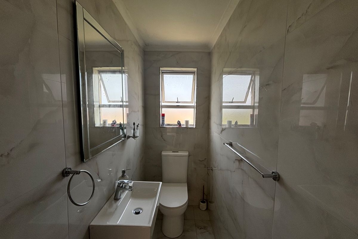 A modern, compact bathroom featuring floor-to-ceiling marble-look tiles, a wall-mounted basin, and a toilet, finished with polished chrome fixtures.