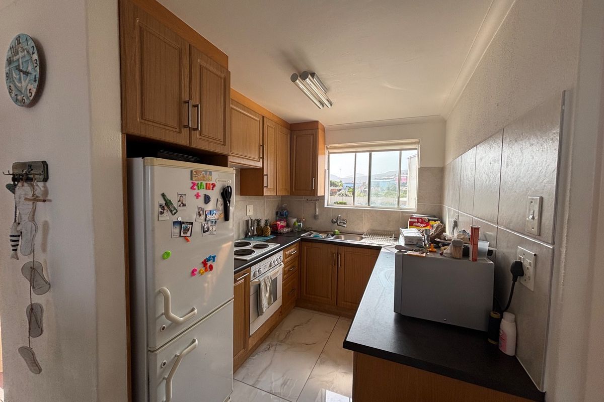 A functional kitchen featuring wood-finish cabinetry, dark laminate countertops, tiled backsplash, and integrated cooking appliances with tiled flooring.