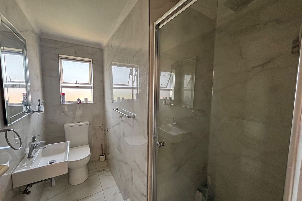 Modern bathroom featuring marble-look wall and floor tiles, a wall-mounted basin, toilet, and a glass-enclosed shower.