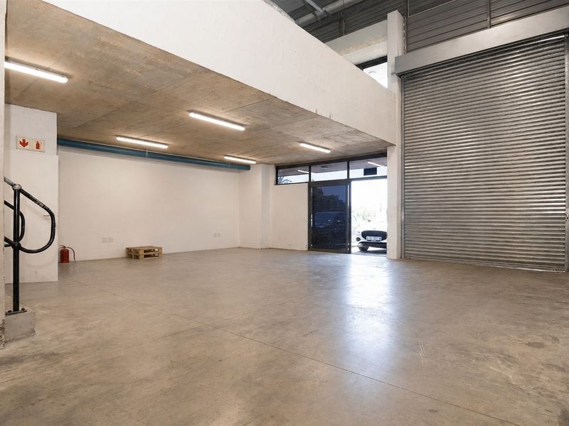 Spacious commercial utility or warehouse space featuring high concrete ceilings, polished concrete flooring, and a large industrial roller shutter door for easy access.
