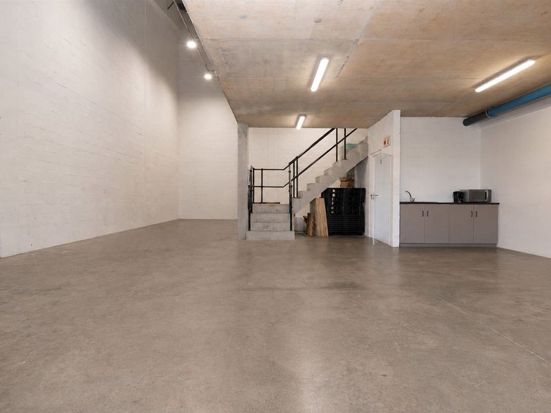 Spacious commercial utility area featuring polished concrete floors, exposed concrete ceiling, a built-in kitchenette, and a staircase leading to an upper level.