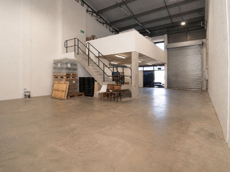 Spacious commercial warehouse unit featuring high ceilings, concrete flooring, a functional mezzanine level, and a large roller shutter door for easy access.