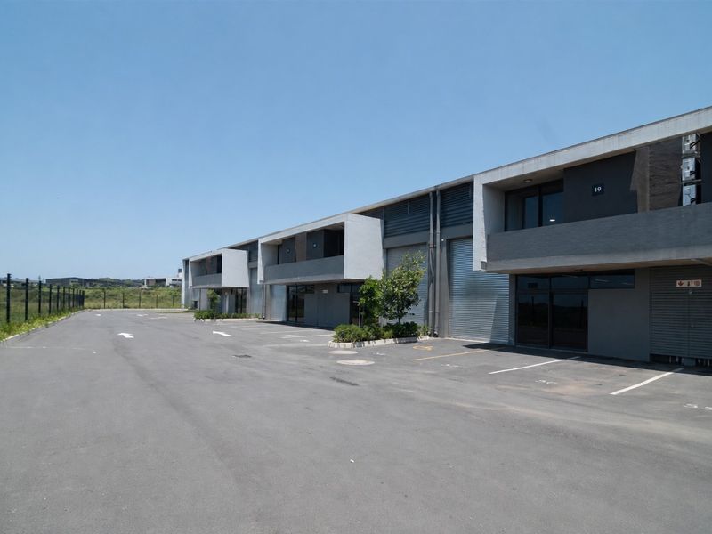 Modern commercial industrial park featuring multiple units with roller shutter doors, paved parking area, and contemporary concrete and metal facade design.