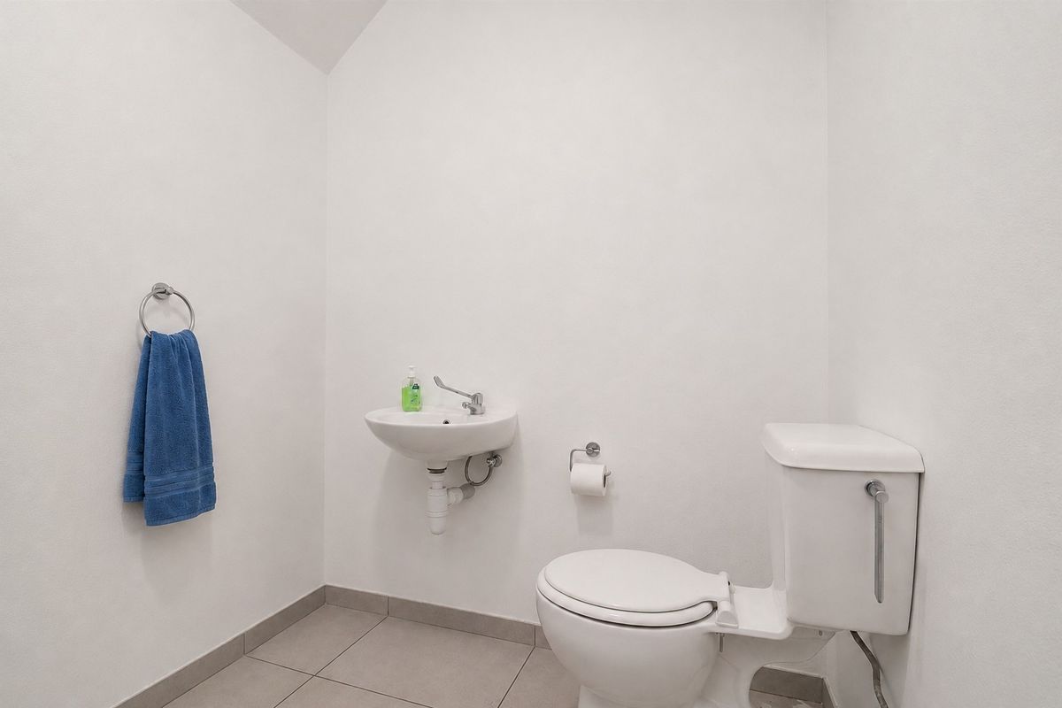 A clean and functional guest bathroom featuring a wall-mounted basin, a standard toilet, and neutral tiled flooring.
