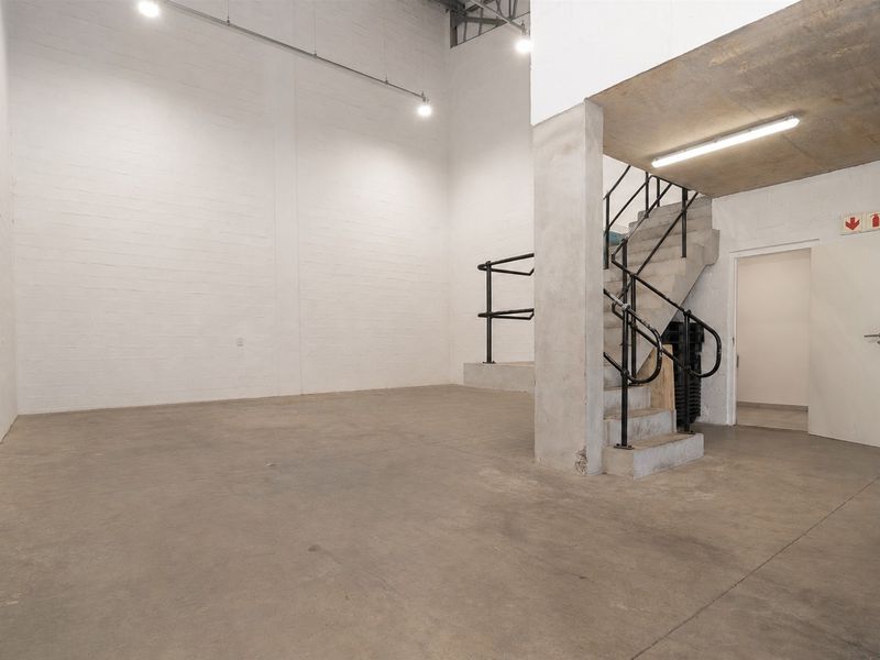 Spacious industrial utility area featuring concrete flooring, exposed structural elements, and a concrete staircase with metal handrails, suitable for various commercial uses.