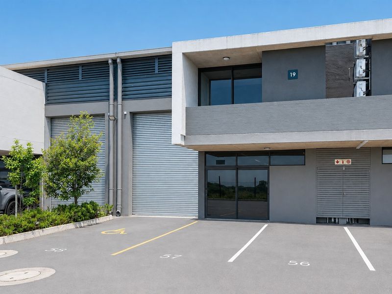 Modern commercial unit featuring a concrete facade, roller shutter doors, and dedicated asphalt parking bays in a well-maintained business park setting.