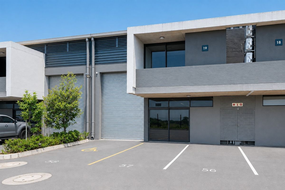 Modern commercial unit featuring a concrete facade, roller shutter doors, and dedicated asphalt parking bays in a well-maintained business park setting.