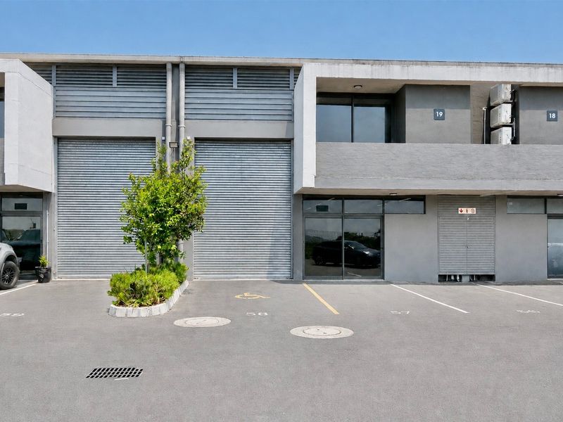 Front elevation of a commercial industrial unit featuring roller shutter doors, dedicated parking bays, and modern concrete facade finishes.