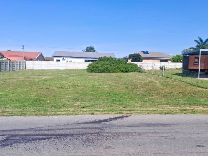 A vacant residential plot featuring a level grass lawn, enclosed by precast concrete boundary walls, with an existing metal carport structure on the side.