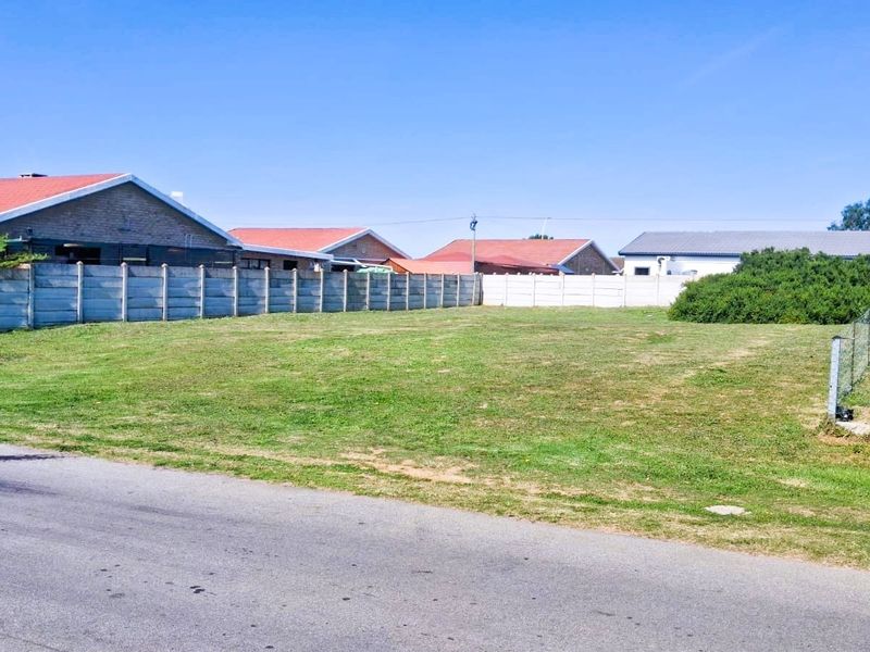 A vacant residential plot featuring a level grass surface, enclosed by precast concrete boundary walls and wire fencing, with direct street access.