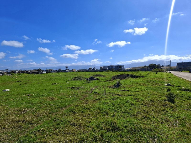 A view of a vacant residential plot of land with grass cover, situated in a developed neighborhood with mountain views in the distance.