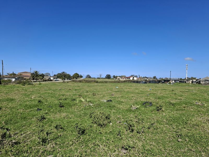A wide-angle view of a vacant residential plot featuring open grassland with surrounding neighborhood infrastructure visible in the distance.