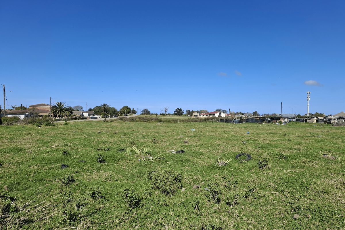A wide-angle view of a vacant residential plot featuring open grassland with surrounding neighborhood infrastructure visible in the distance.