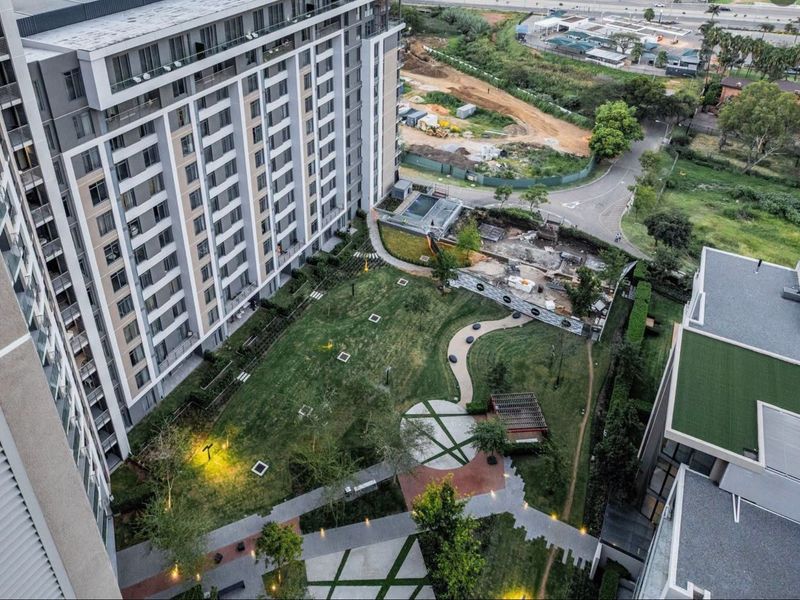 Aerial view of the apartment complex grounds featuring a landscaped garden, paved walkways, outdoor lighting, and a pergola area.
