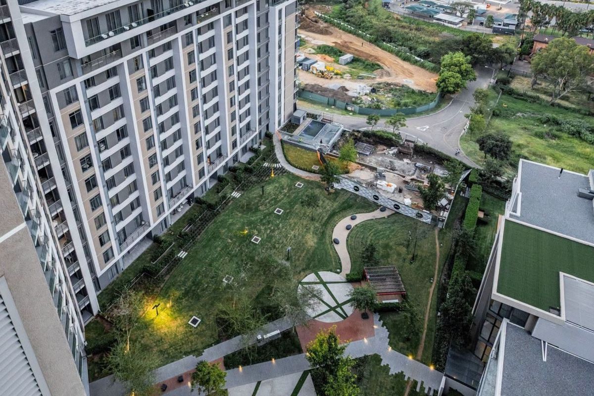 Aerial view of the apartment complex grounds featuring a landscaped garden, paved walkways, outdoor lighting, and a pergola area.