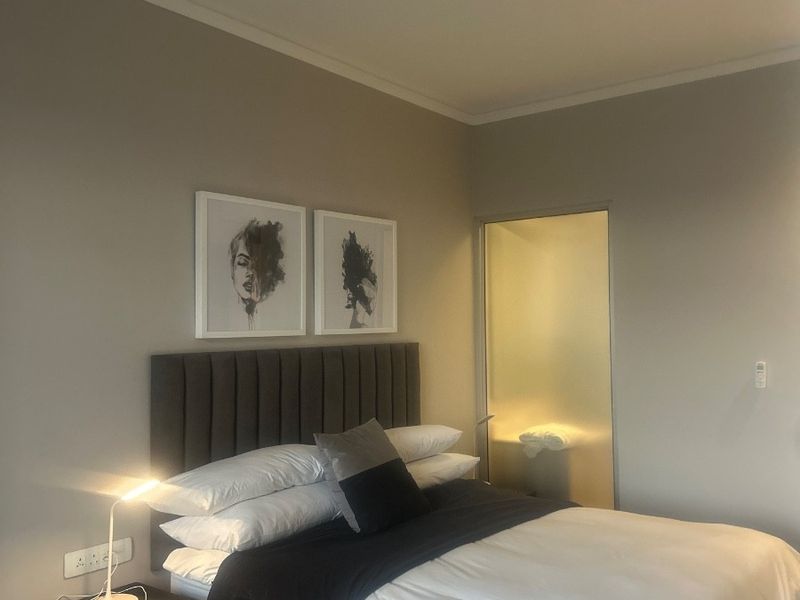 A well-maintained bedroom featuring neutral wall tones, a frosted glass door leading to an en-suite, and modern electrical fixtures.