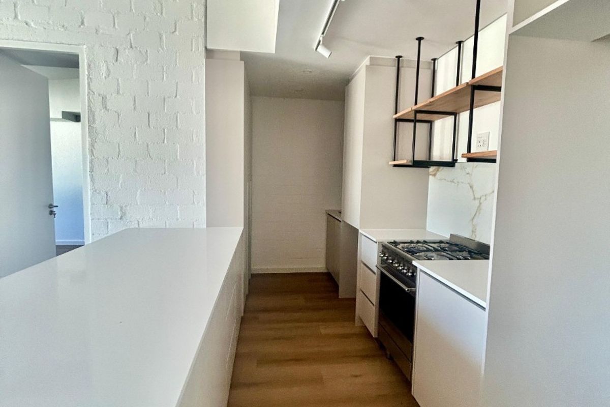 Modern kitchen featuring white cabinetry, stone countertops, gas stove, oven, and stylish floating shelves with track lighting and exposed brick accents.
