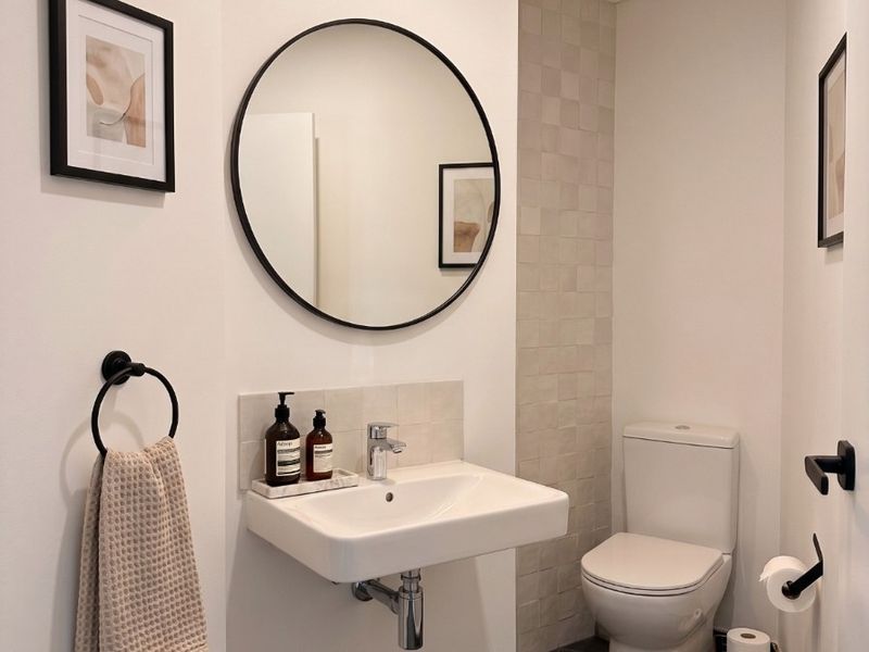 A modern, well-maintained bathroom featuring a wall-mounted basin, chrome fixtures, and neutral tiled finishes, creating a clean and contemporary aesthetic.