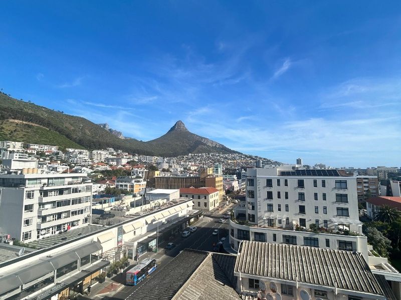 Elevated urban view overlooking the city streets and surrounding buildings with a prominent mountain peak in the background.