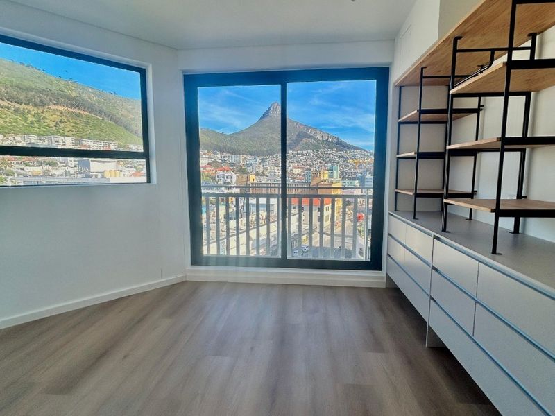 Bright bedroom featuring modern laminate flooring, built-in storage shelving, and large sliding glass doors offering expansive mountain and city views.
