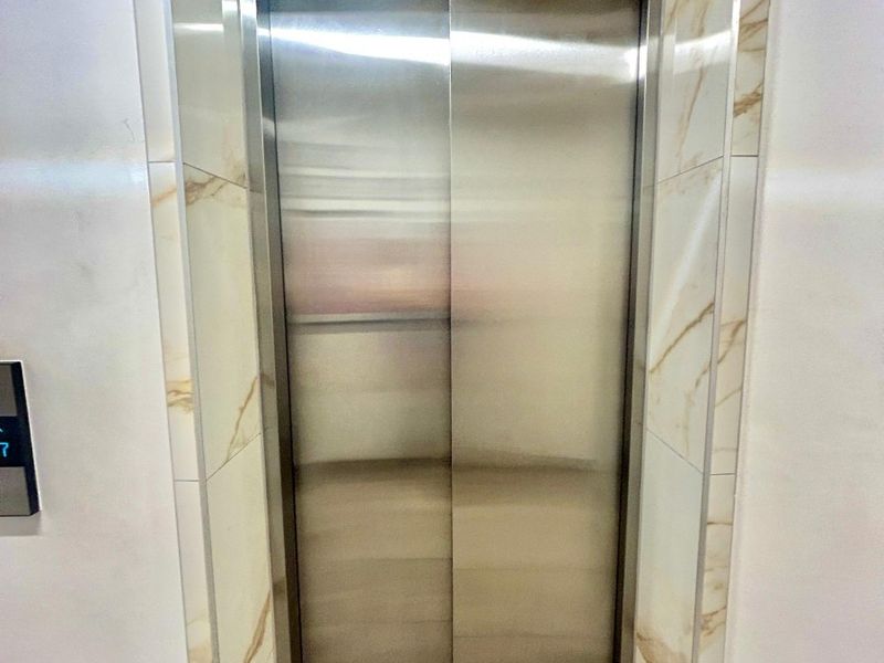 A modern elevator entrance featuring stainless steel doors framed by elegant marble-look wall tiles.