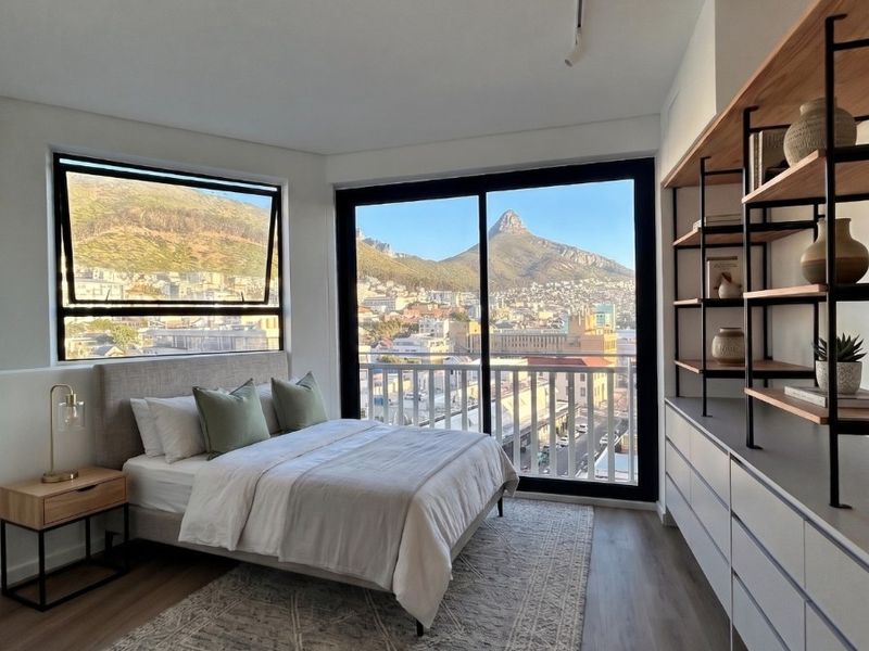 Modern bedroom featuring built-in shelving, laminate flooring, and large windows offering expansive mountain and city views with access to a private balcony.