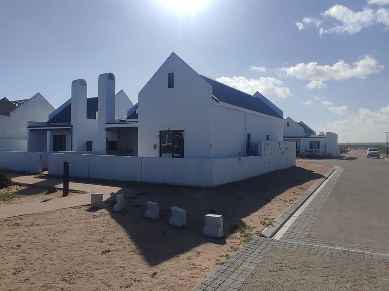 A view of a coastal residential development featuring white gabled houses with prominent chimneys and paved access roads.