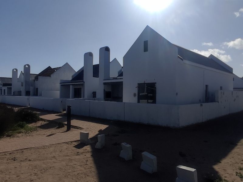 A row of white gabled houses under construction, featuring prominent chimney stacks and surrounding boundary walls in a coastal estate setting.