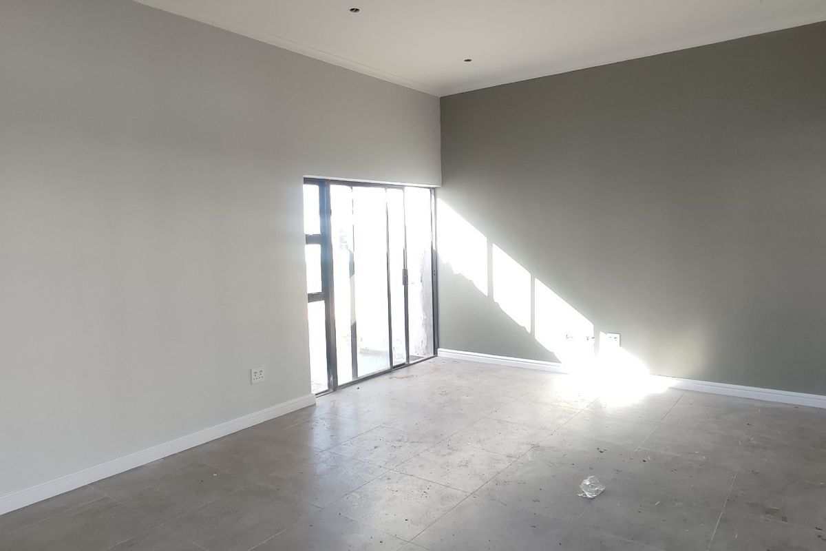A spacious, empty living area featuring neutral-toned walls, large sliding glass doors for natural light, and modern tiled flooring.