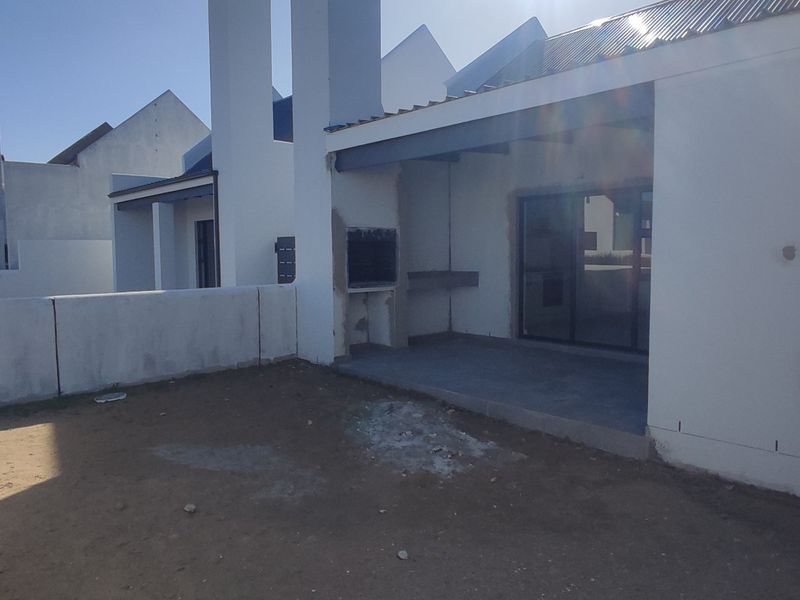 Rear exterior view featuring a covered patio with a built-in braai, sliding glass doors, and an unfinished garden area.