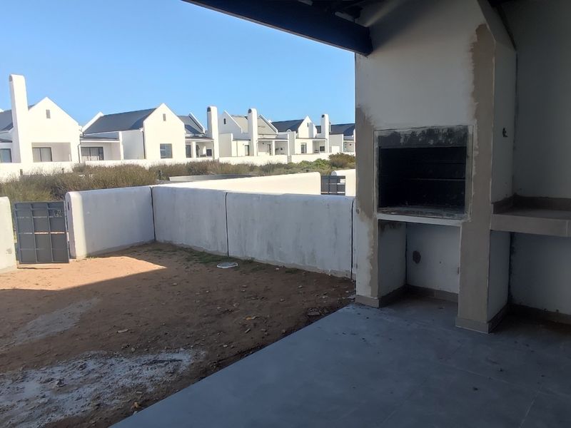 Covered patio area featuring a built-in braai and concrete counter, currently in an unfinished state with an adjacent unpaved garden space.