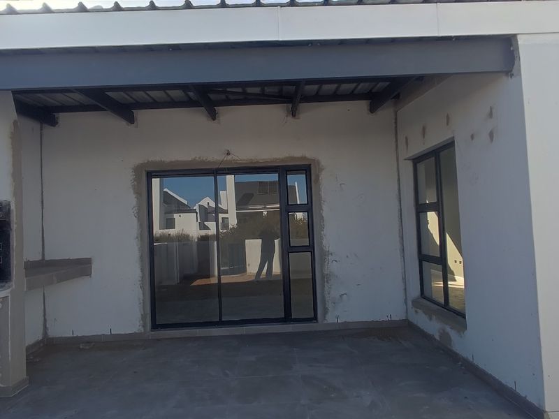 An unfinished covered patio area featuring a built-in braai, sliding glass doors, and tiled flooring, awaiting final plastering and finishing touches.