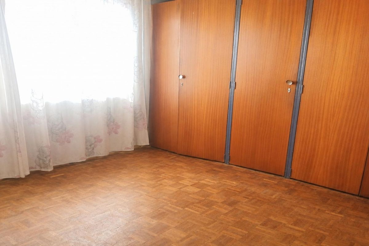 A bedroom featuring classic parquet flooring and extensive built-in wooden cupboards, offering a functional and neutral space ready for updates.
