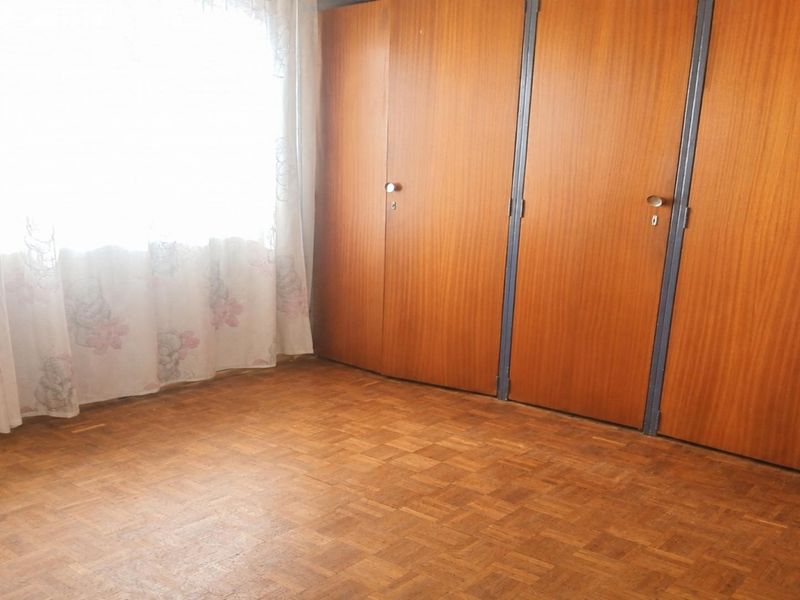 A bedroom featuring classic parquet flooring and extensive built-in wooden cupboards, offering a functional and neutral space ready for updates.
