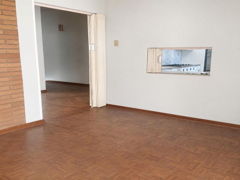Spacious living area featuring parquet flooring, a brick feature wall, and a convenient serving hatch connecting to the kitchen.