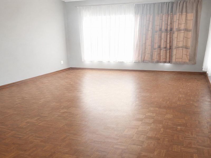A spacious, empty living room featuring classic parquet flooring and large windows with installed curtain rails, offering a blank canvas for interior design.