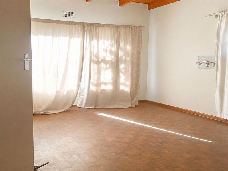 A bright, empty living room featuring classic parquet flooring and exposed timber ceiling beams, offering a versatile space ready for personalization.