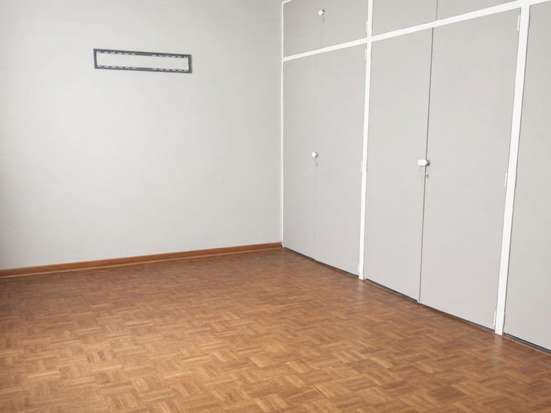An empty bedroom featuring classic parquet flooring and extensive built-in cupboard storage, providing a clean and functional space.
