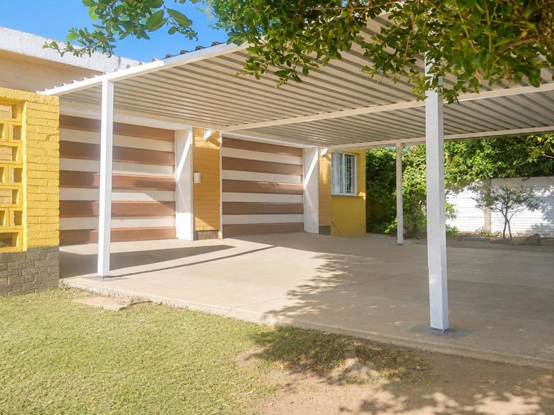 A spacious double carport with a concrete driveway and brick facade, providing covered parking and access to the garage.