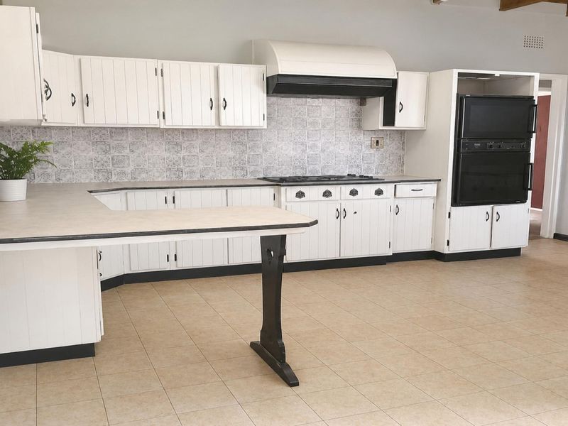 Spacious kitchen featuring white cabinetry, built-in oven, gas hob, extractor fan, and tiled flooring, offering a functional layout ready for modern updates.