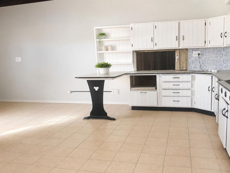 A functional kitchen featuring white built-in cabinetry, tiled backsplash, integrated oven, and a breakfast bar, offering a clean and practical layout.
